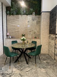 masă rotundă cu blat din granit natural și patru scaune din catifea verde, într-un spațiu decorat cu piatră naturală